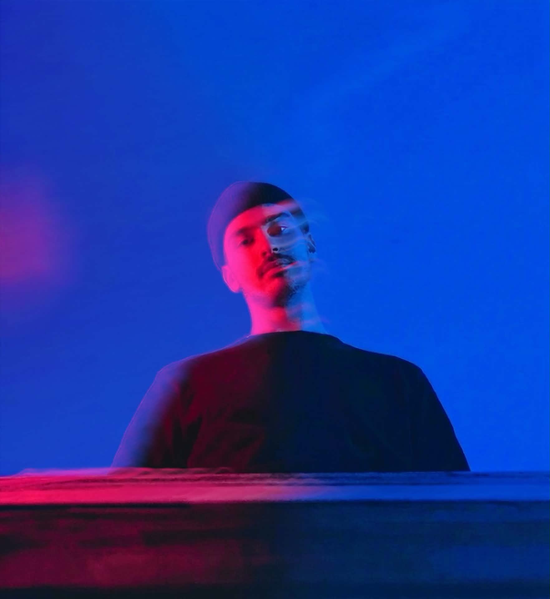 Portrait of hun in a beanie under blue and red light, the motion of the shot smearing his features.